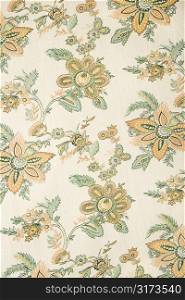 Close-up of vintage fabric with golden flowers and green leaves printed on polyester.