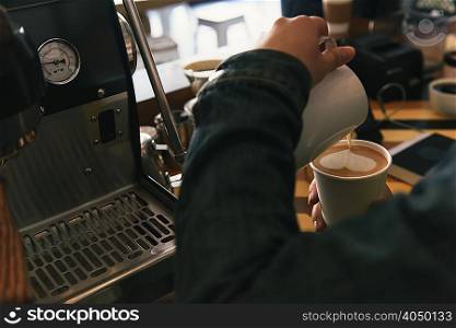 Close up of waiter pouring heart shape milk into coffee cup at coffee shop counter