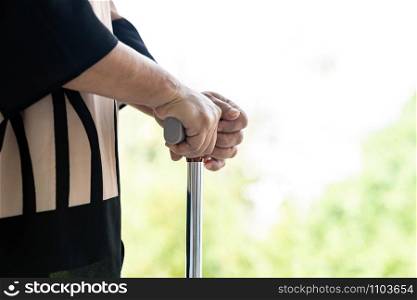 Close up of walking stick or walking cane staff using by elderly senior female hand in domestic living room - recovery and rehabilitation concept