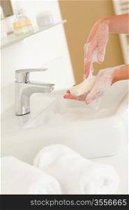 Close-up of washing hands with soap above bathroom sink