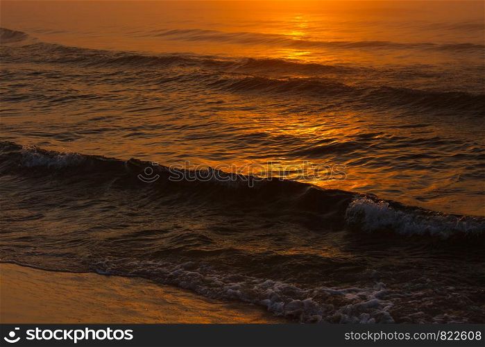 Close up of waving sea water during sunset in orange and gold shades. Dark atmosphere. Waving sea during sunset