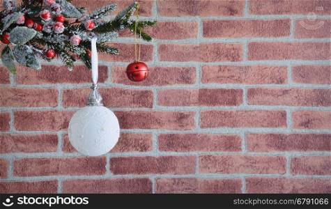 Close up of white Christmas ball at left side hanging on decorative fir branch against of brick wall