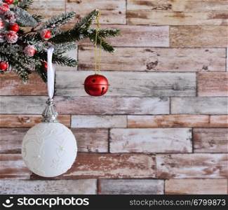 Close up of white Christmas ball at left side hanging on decorative fir branch against of wooden wall