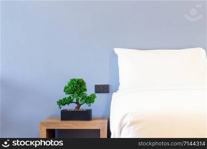 Close-up of white pillow on bed decoration with green tree in flowerpots in hotel bedroom interior.