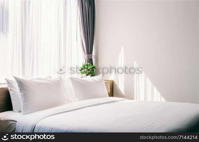 Close-up of white pillow on bed decoration with light lamp and green tree in flowerpots in hotel bedroom interior.