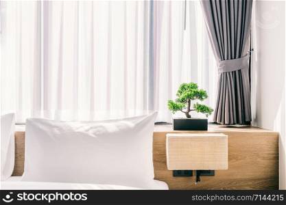 Close-up of white pillow on bed decoration with light lamp and green tree in flowerpots in hotel bedroom interior.