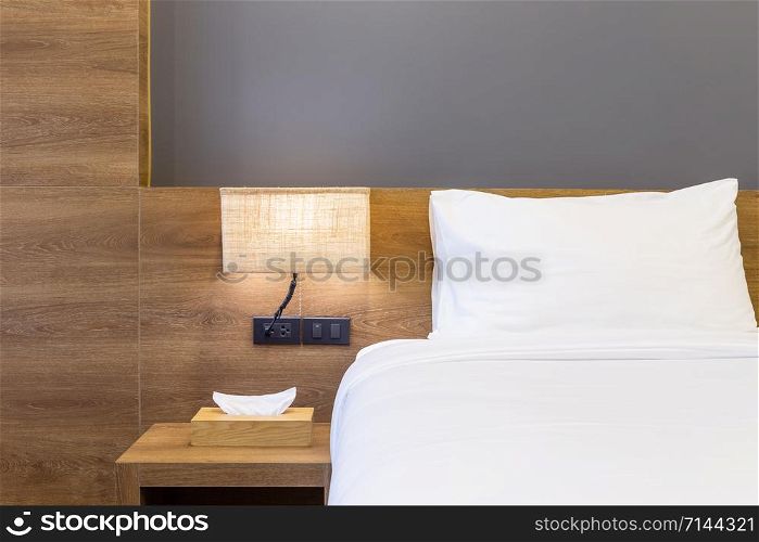 Close-up of white pillow on bed decoration with light lamp and tissue box in hotel bedroom interior.