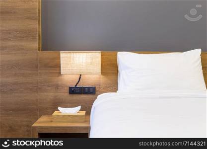 Close-up of white pillow on bed decoration with light lamp and tissue box in hotel bedroom interior.