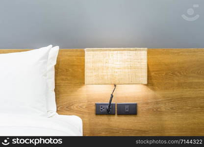 Close-up of white pillow on bed decoration with light lamp in hotel bedroom interior.