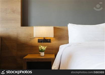 Close-up of white pillow on bed decoration with light lamp in hotel bedroom interior.