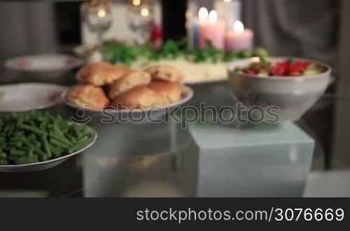 Close up of woman&acute;s hand serving roasted turkey with apples and broccoli on platter on Thanksgiving table, decorated with candles and dishes.