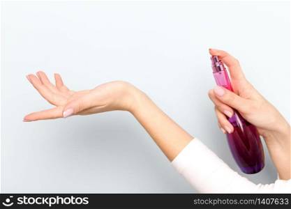 Close up of woman applying/spraying perfume on her wrist over light blue background.