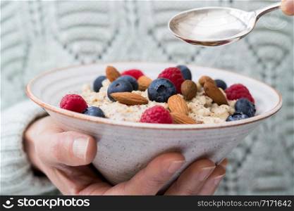 Close Up Of Woman Eating Bowl Of Porridge with Fruit And Nuts For Healthy Breakfast