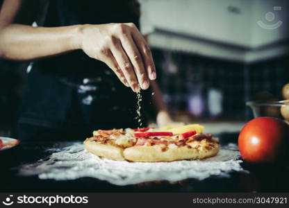 Close up of woman hand putting oregano over tomato and mozzarella on a pizza. Cooking concept