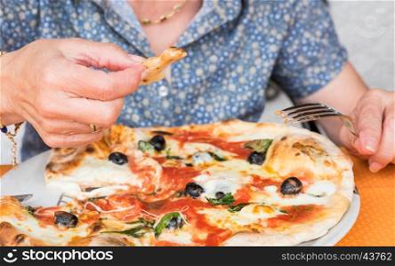 Close-up of woman hands cutting and eats pizza outside at restaurant, selective focus.