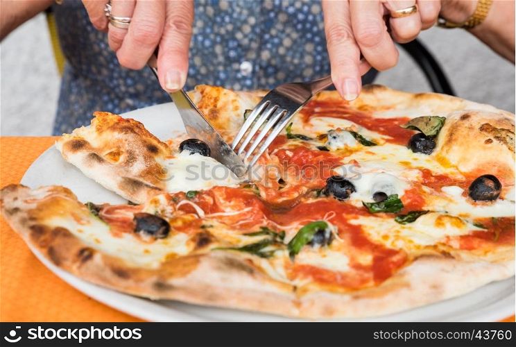 Close-up of woman hands cutting pizza outside at restaurant, selective focus.