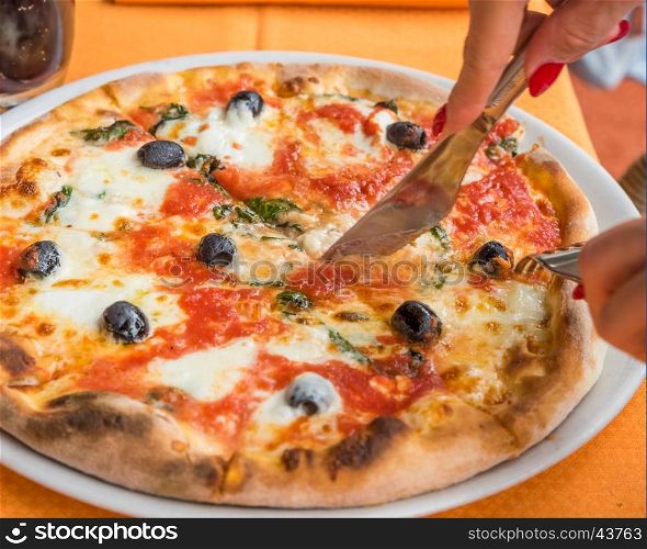 Close-up of woman hands cutting pizza outside at restaurant, selective focus.