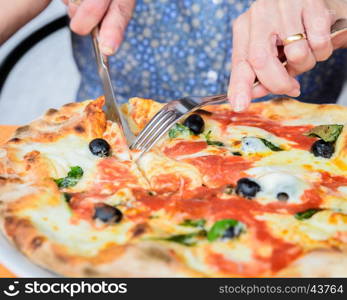 Close-up of woman hands cutting pizza outside at restaurant, selective focus.