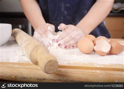 Close-up of woman hands knead dough on wooden table with flour, eggs and rolling pin. Cooking concept.