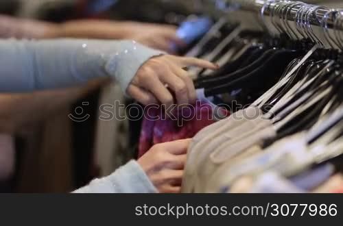 Close up of woman hands on clothes hangers in store buying clothes. Senoir beautiful women shopping in fashion mall, choosing new clothes, looking through hangers with different casual colorful garments on hangers.