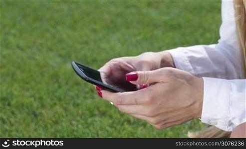 Close up of woman hands with the smartphone touching screen and using app outside in the park