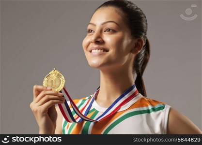 Close-up of woman holding gold medal isolated over gray background