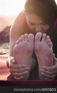 Close up of woman holding her feet practicing yoga at dawn