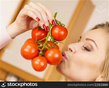 Close up of woman holding small cherry tomatoes on branch next to her face, thinking of eating it.. Woman hand holding tomates