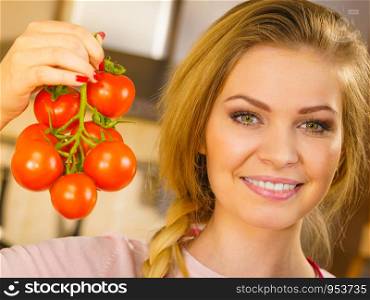 Close up of woman holding small cherry tomatoes on branch next to her face, thinking of eating it.. Woman hand holding tomates