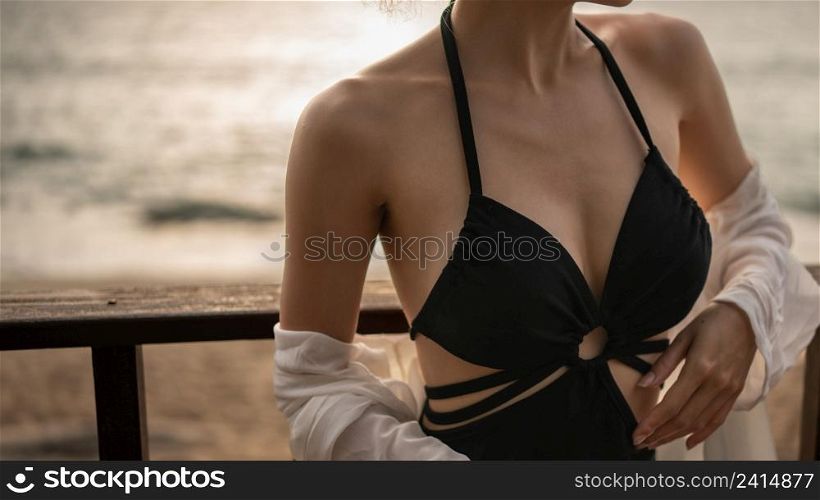 Close up of woman in black dress standing on a balcony, ocean view.