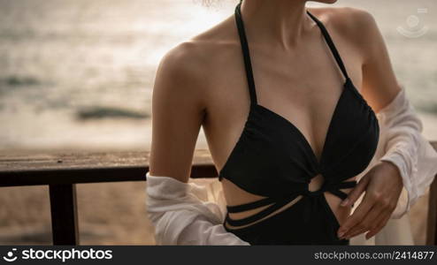 Close up of woman in black dress standing on a balcony, ocean view.