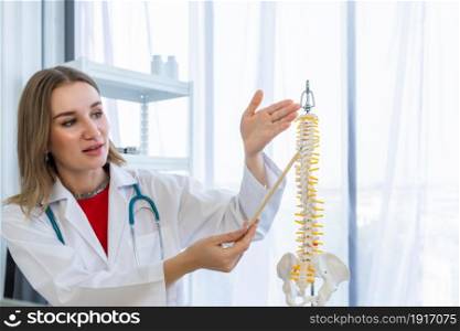 Close-up of woman medical doctor therapeutic with stethoscope pointing on spine model with positive emotions in hospital background.