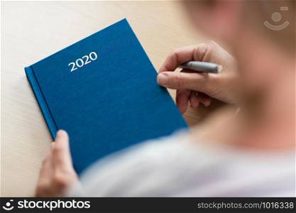 Close Up Of Woman Opening New Year 2020 Diary On Table