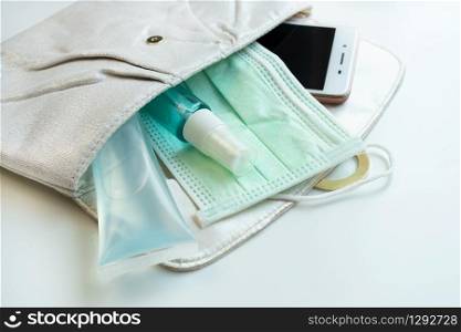 Close up of woman pouch with smart phone, sanitizer, alcohol spray and protective face mask. Health care concept.