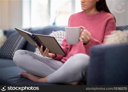 Close Up Of Woman Relaxing On Sofa At Home Reading Journal