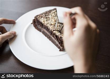Close-up of woman&rsquo;s hand holding fork to chocolate pastry