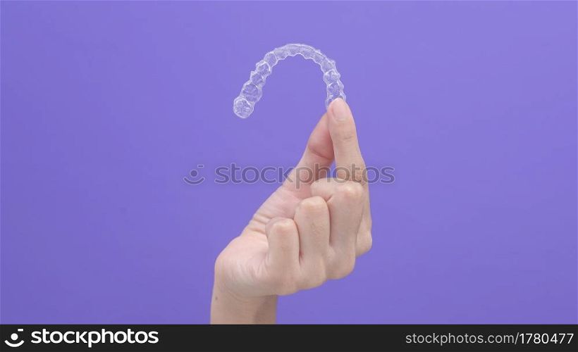 close up of woman&rsquo;s hand holding invisalign braces in studio, dental healthcare and Orthodontic concept.