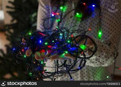 Close-up of woman&rsquo;s hands with red, green and blue colored lights to decorate the Christmas tree. Close-up of woman&rsquo;s hands with colored lights to decorate the Christmas tree