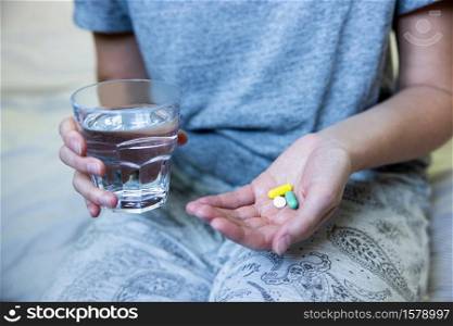 Close Up Of Woman Sitting On Bed Wearing Pyjamas Taking Medication With Glass Of Water