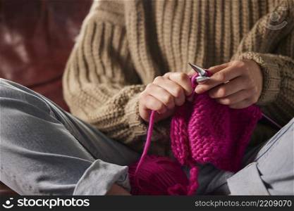Close Up Of Woman Sitting On Sofa At Home Knitting Jumper With Pink Wool