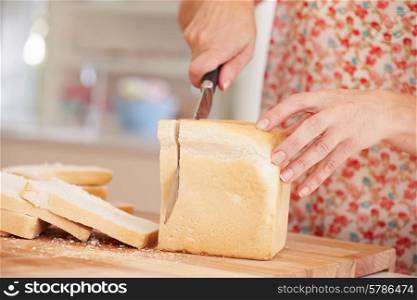 Close Up Of Woman Slicing Loaf Of Bread In Kitchen