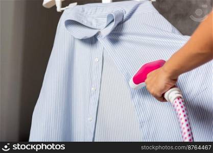 Close up of woman using electric hand steam generator while it is hot and steam comes out for clothes shirt at house, Household & home equipment for housework, concept of linen care