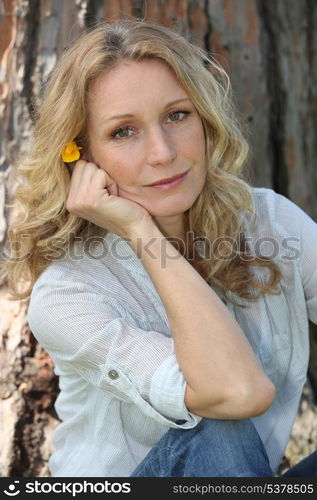 Close-up of woman with flower in hair sitting in front of tree