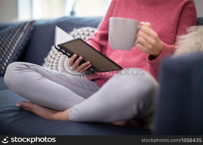 Close Up Of Woman With Hot Drink Relaxing On Sofa At Home Reading Journal