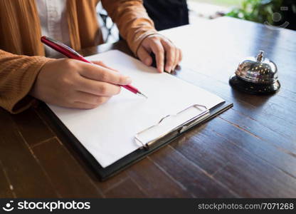 Close up of women putting signing and filling up form at hotel reception.