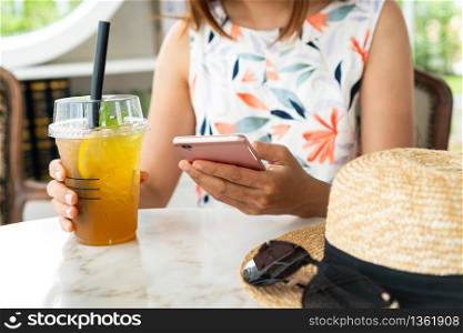 Close up of women&rsquo;s hands holding drinks while using mobile phone in cafe.