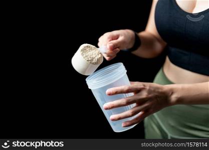Close up of women with measuring scoop of whey protein and shaker bottle, preparing protein shake.