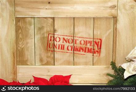 Close up of wooden box with red text stating do not open until Christmas. Partial poinsettia and evergreen.