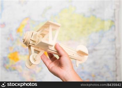Close-up of wooden toy plane in children’s hands on world map background in kids room at home. Childhood dream imagination and Travel concepts.