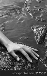 Close up of young adult Asian female hand in water on rocks.